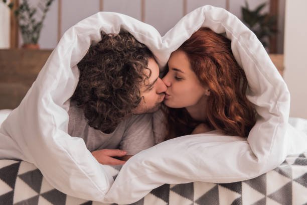 beautiful couple is kissing while lying in bed wrapped in blanket beautiful couple is kissing while lying in bed wrapped in blanket
